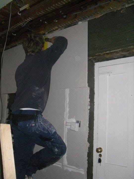 An electrician working high on a wall beside a door during a renovation